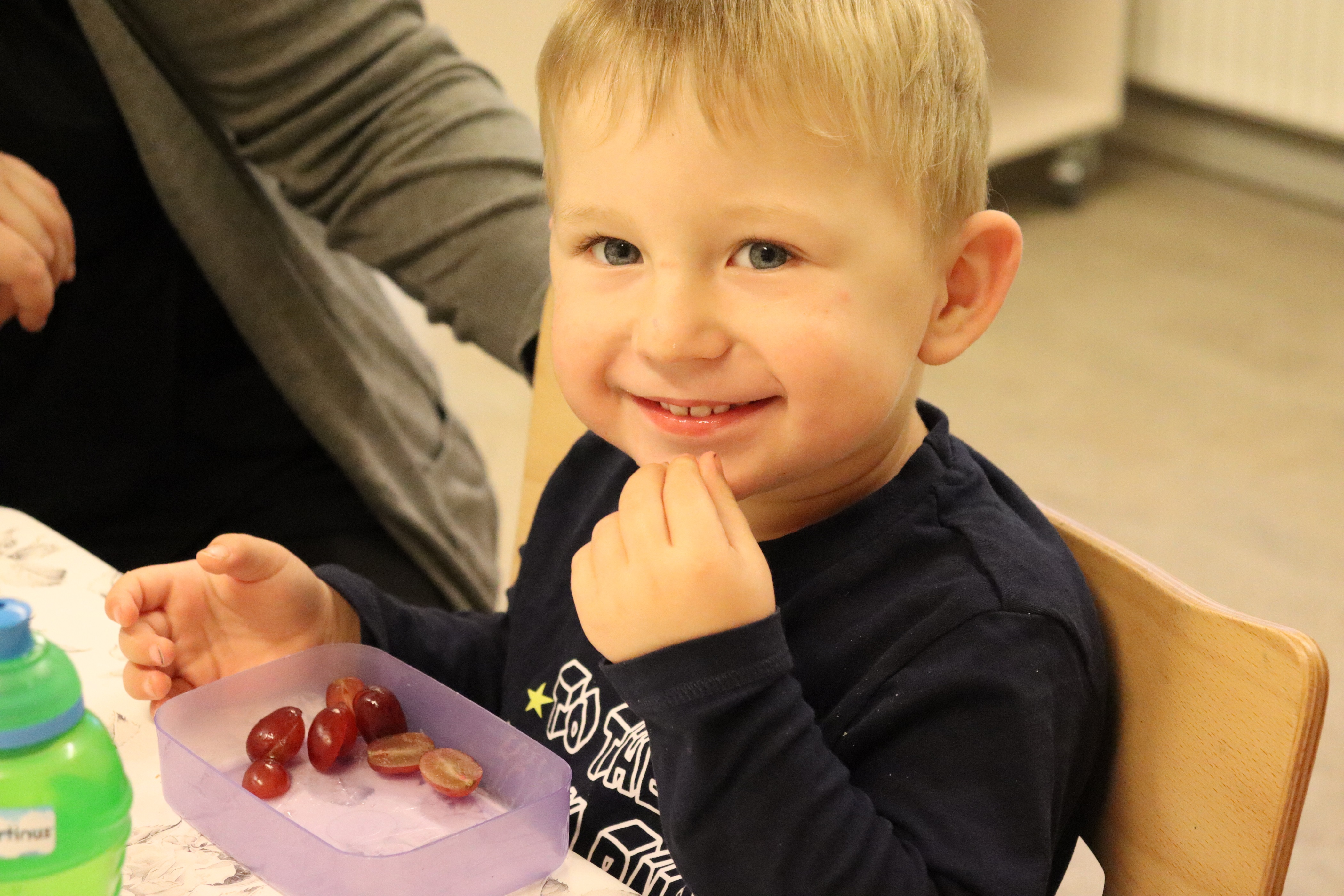 Vuggestuebarn spiser frugt imens han smiler stort