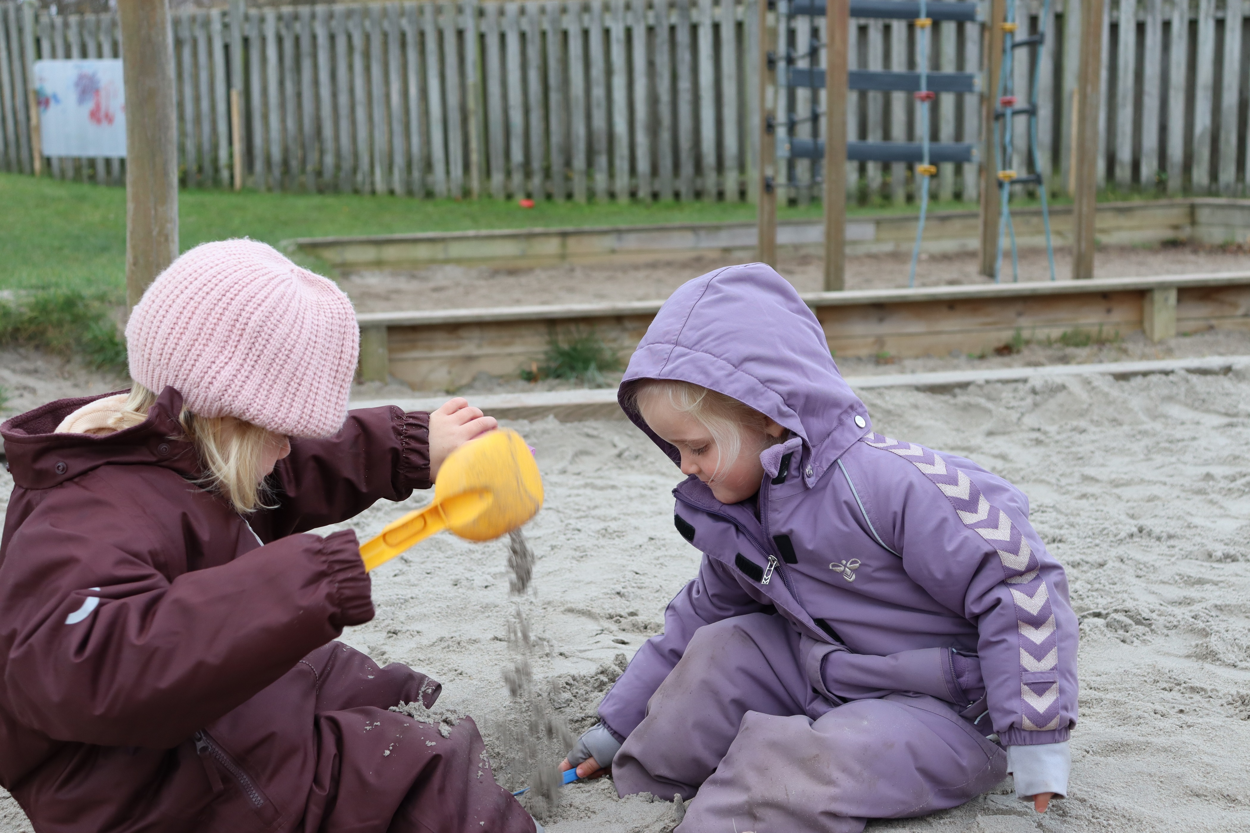 To piger leger i sandkassen med sand og sandkasseting