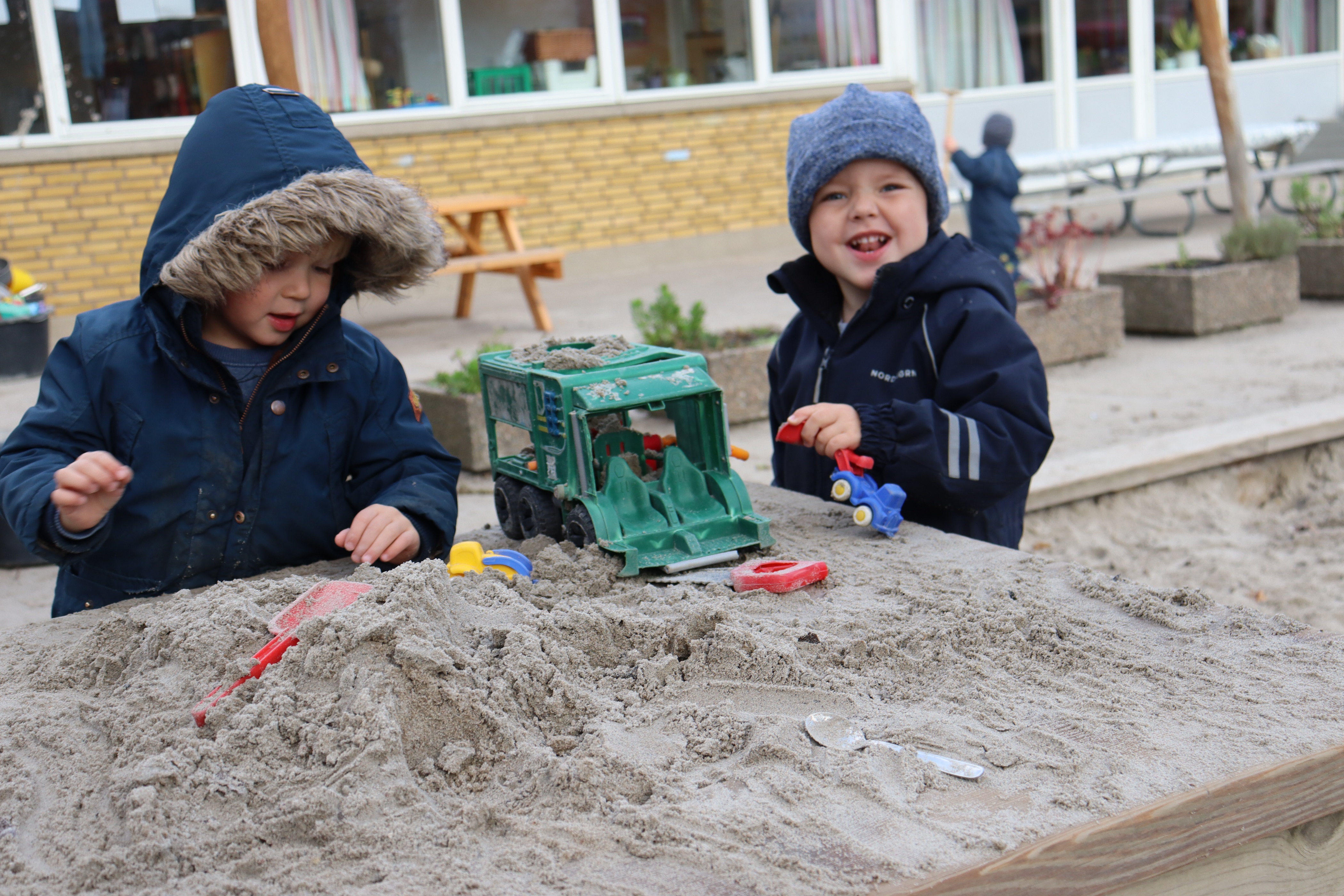 To drenge leger i sandkasse med maskiner