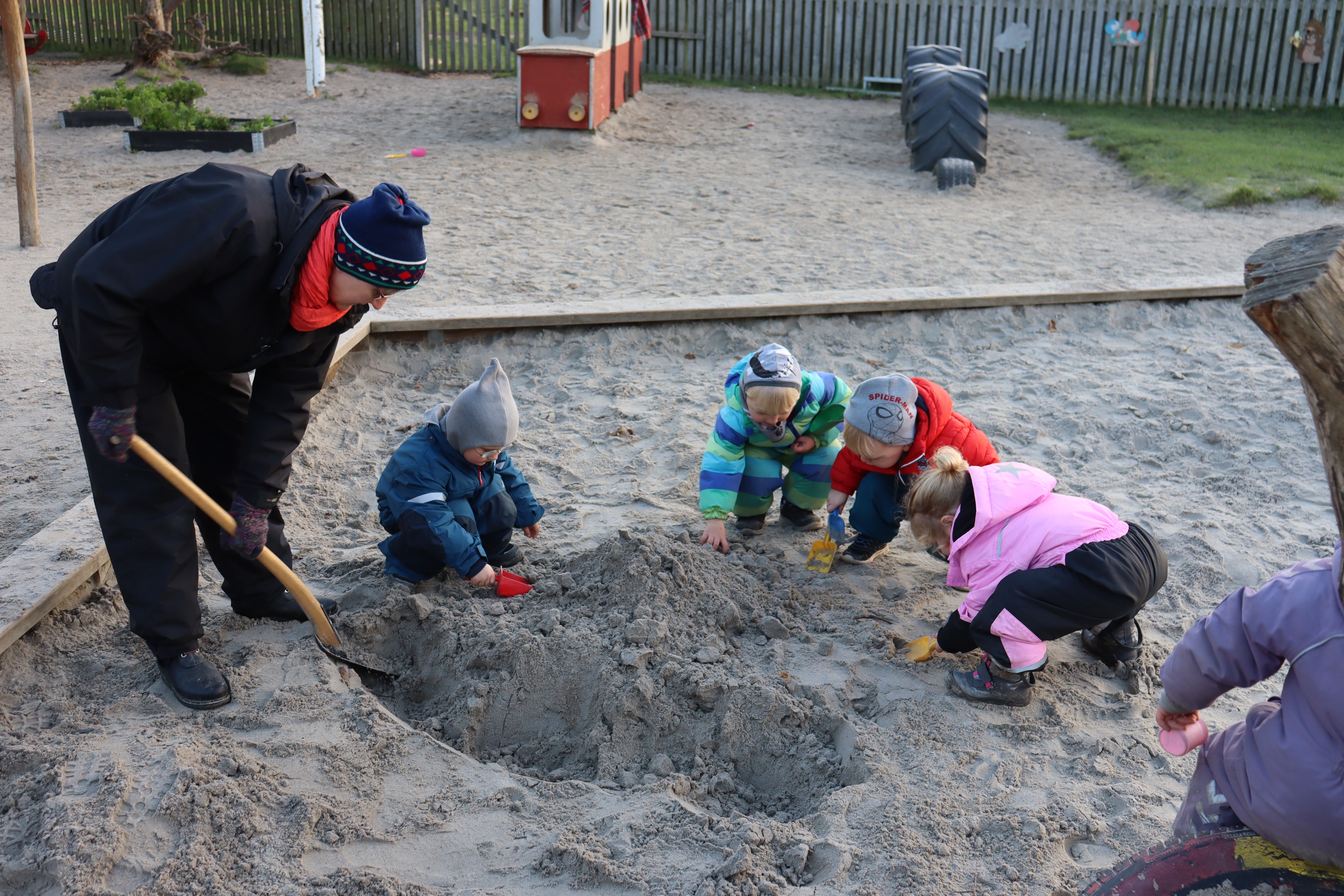 Pædagog hjælper med at grave i sandkassen med børn omkring sig